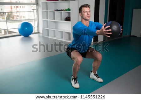 Handsome Young Man Doing Squad With Medicine Ball As Part Of Bodybuilding Training