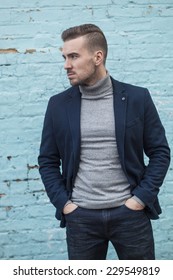 Handsome Young Man Dresses In Jeans And Blue Blazer Posing Against Painted Blue Brick Wall