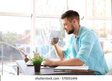 Handsome Young Man Drinking Coffee While Working With Laptop At Home