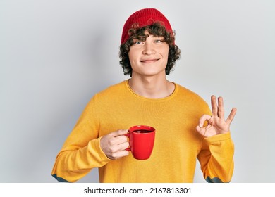 Handsome young man drinking a cup coffee doing ok sign with fingers, smiling friendly gesturing excellent symbol  - Shutterstock ID 2167813301