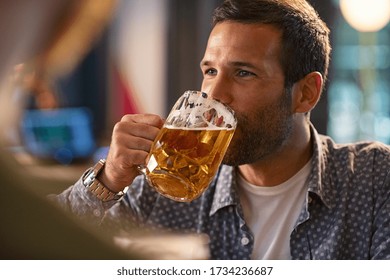 Handsome young man drinking a pint of beer. Cheerful mid man in casual clothing feeling relaxed while enjoying draft beer in bar. Middle aged guy take a sip from his drink at pub during the night. - Powered by Shutterstock