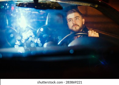 Handsome Young Man Driving His Modern Sport Car, Looking Back In The Mirror, At Night