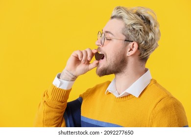 Handsome Young Man Eating Chocolate Candy On Color Background