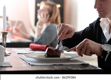 A Handsome Young Man Eating Delicious Meat Cutlet With A Knife And Fork At A Table Elegantly Served