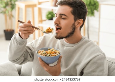 Handsome young man eating tasty cereal rings in living room - Powered by Shutterstock