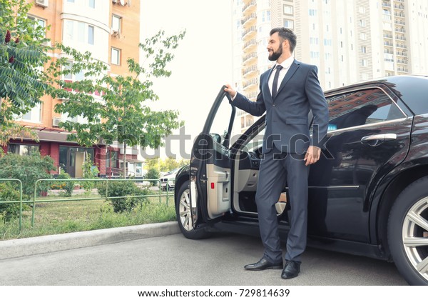 Handsome young man in elegant suit standing near\
car outdoors