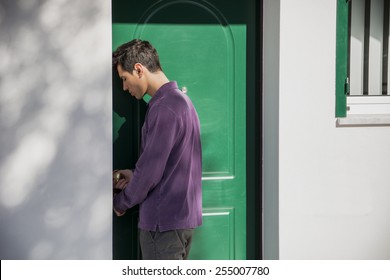 Handsome Young Man Entering Home Through A Green Door In An Exterior Wall Of A House 