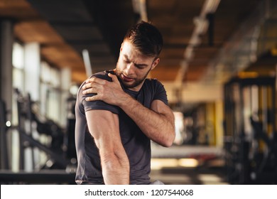 Handlicher junger Mann, der die Schmerzen in der Schulter im Fitnessraum spürt