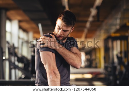 Handsome young man feeling the pain in shoulder at the gym