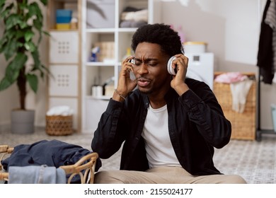 Handsome Young Man Folds Clean Clothes Sorts Laundry Before Putting It In Washing Machine College Student Sits On Bathroom Floor Listening To Music On Wireless Headphones With Eyes Closed.