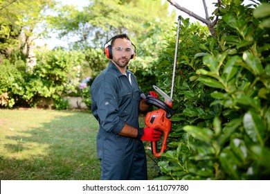 handsome young man gardener trimming hedgerow in a garden park outdoor - Shutterstock ID 1611079780