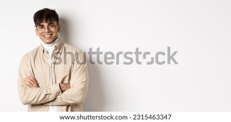 Handsome young man in glasses cross arms on chest, smiling at camera carefree, standing on white background.