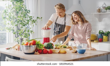 Handsome Young Man in Glasses Wearing Apron and Beautiful Girl are Making A Smoothie in the Kitchen. Happy Couple are Preparing Healthy Organic Beverage. Male and Female at Home on a Sunny Day. - Powered by Shutterstock