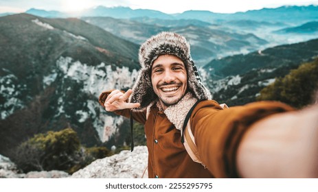 Handsome young man with hat and backpack taking selfie with smart mobile phone device outside - Hiker taking self portrait on the top of the mountain - Travel, sport, technology and life style concept - Powered by Shutterstock