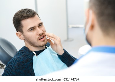 Handsome young man having toothache sitting in a dental chair. Professional dentist helping his male patient in pain copyspace painful treatment curing cure help advice painful dentistry medical