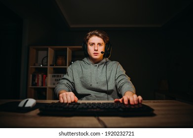 Handsome young man in headset on his head playing video games at home on the computer and looking at the camera with a serious face. Night gaming in the bedroom of the house. - Powered by Shutterstock