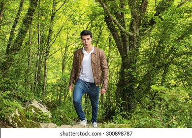 Handsome young man hiking in lush green mountain scenery, walking up the hill, looking at camera