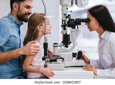 Handsome young man and his little cute daughter are checking the eye vision in modern ophthalmology clinic. Dad and daughter with doctor ophthalmologist.