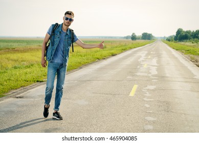 Handsome Young Man Hitchhiker Standing On A Highway. Adventure And Tourism Concept. Jeans Style.