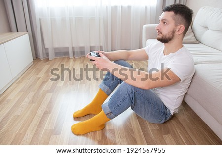 Handsome young man holding controller and playing video games. Spending time at home concept. Adult gamer sitting on sofa at house in living room with joystick in hands.