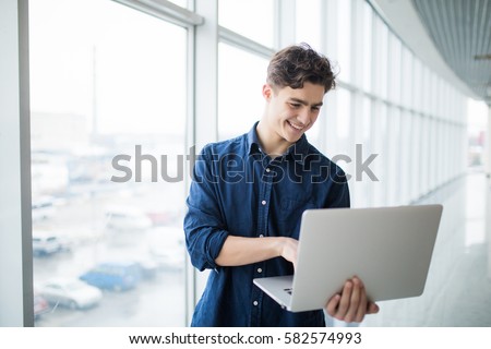 Handsome young man man holding a laptop in hall