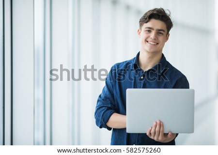 Handsome young man man holding a laptop in hall