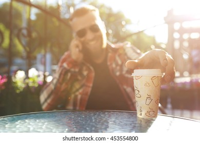 Handsome young man holding mobile phone and drinking coffee while sitting in the rest area of the office. 