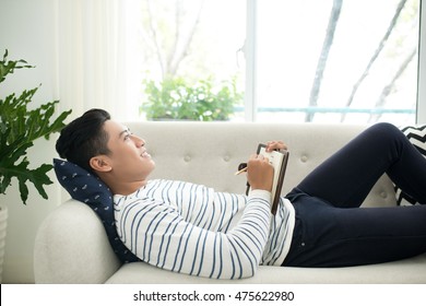Handsome Young Man At Home Writing  Writing Down Thoughts In Journal On Notebook, Sitting On Couch