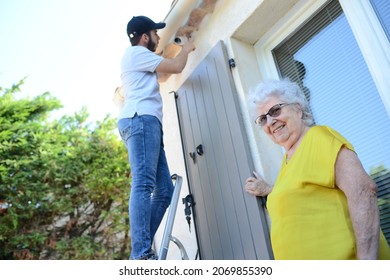 Handsome Young Man Installing House Security Anti Burglary Camera And Siren Alarm In A Senior Woman Home