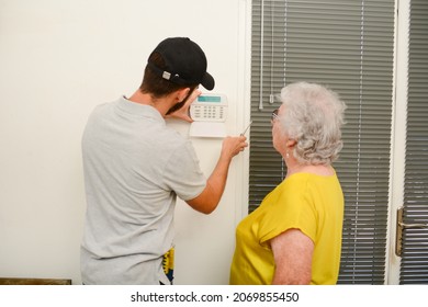 Handsome Young Man Installing House Security Anti Burglary Camera And Siren Alarm In A Senior Woman Home