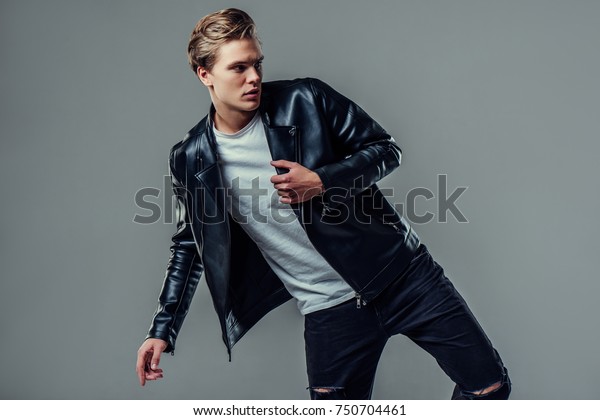Handsome young man isolated.\
Fashionable  man in leather jacket is standing on grey\
background.