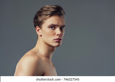 Handsome young man isolated. Portrait of shirtless muscular man is standing on grey background and looking at camera.