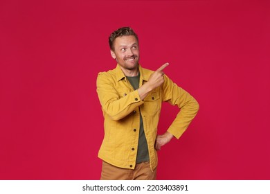 Handsome young man in jeans jacket pointing looking sideways up mock up advertisement isolated on red background. Charming smiling freelancer introduce your business offer.  - Shutterstock ID 2203403891