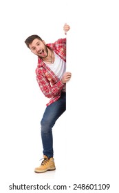 Handsome young man in jeans and lumberjack shirt standing behind white banner and shouting. Full length studio shot isolated on white.