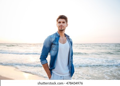 Handsome Young Man In Jeans Shirt Standing On The Beach