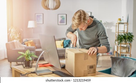 Handsome Young Man In Living Room With Cardboard Box Package, Opening It With Interest, Using Knife.