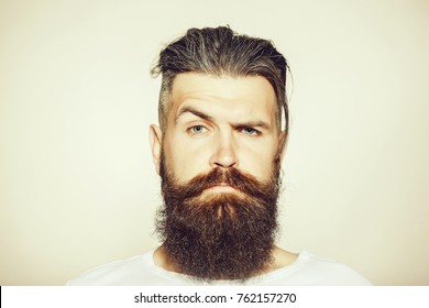 handsome young man with long beard and moustache on serious face with raised eyebrow on grey background in studio