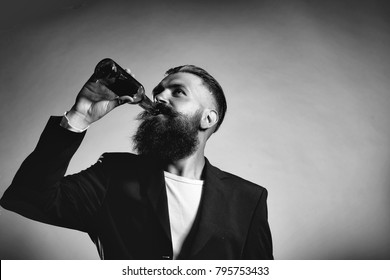 Handsome Young Man With Long Beard And Moustache In Black Jacket Holding Green Glass Beer Bottle In Studio On Grey Background