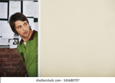 Handsome Young Man Looking Around Corner In Office