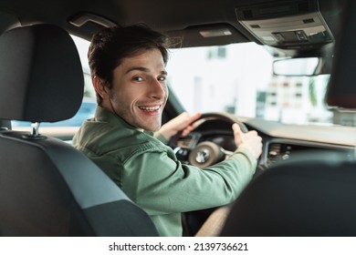 Handsome Young Man Looking Back At Camera, Sitting In Car, Parking Auto, View From Rear Seat. Happy Millennial Guy Buying Automobile At Modern Dealership Store, Copy Space