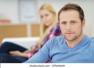 Handsome Young Man Looking Directly At The Camera With A Serious Intense Expression While Relaxing At Home On The Sofa With His Wife