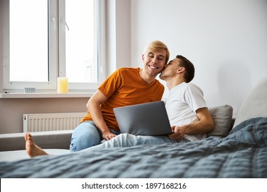 Handsome young man looking at notebook display and smiling while loving boyfriend kissing his cheek - Shutterstock ID 1897168216