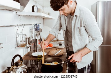 Handsome Young Man Making Eggs On Breakfast In Kitchen At Home