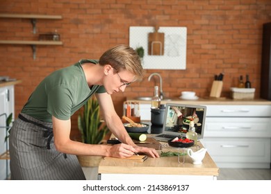 Handsome young man making notes from cooking video tutorial in kitchen