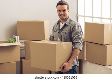 Handsome young man is moving, holding a cardboard boxes, looking at camera and smiling - Shutterstock ID 410331058