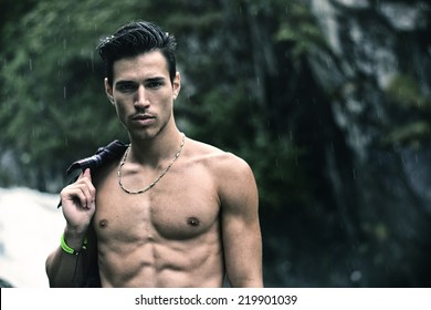 Handsome young man near mountain waterfall shirtless, under rain - Powered by Shutterstock