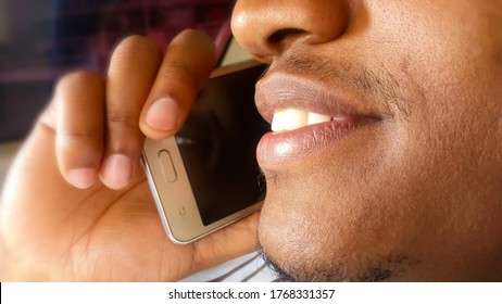 Handsome Young Man On A Phone Call. Listening. Close Up. Side View. Attentive, Smiling With His White Teeth Showing. African Man With Light Skin. Holding, Using A Smartphone With One Hand To His Ear.