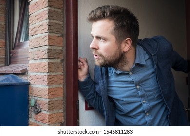 Handsome Young Man Opening Door Looking On What His Neighbor Is Doing Suspecting Something.