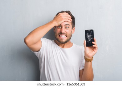 Handsome young man over grey grunge wall showing broken smartphone screen stressed with hand on head, shocked with shame and surprise face, angry and frustrated. Fear and upset for mistake. - Powered by Shutterstock