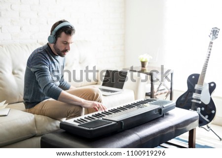 Handsome young man playing music and composing a song with electric piano while sitting in living room at home